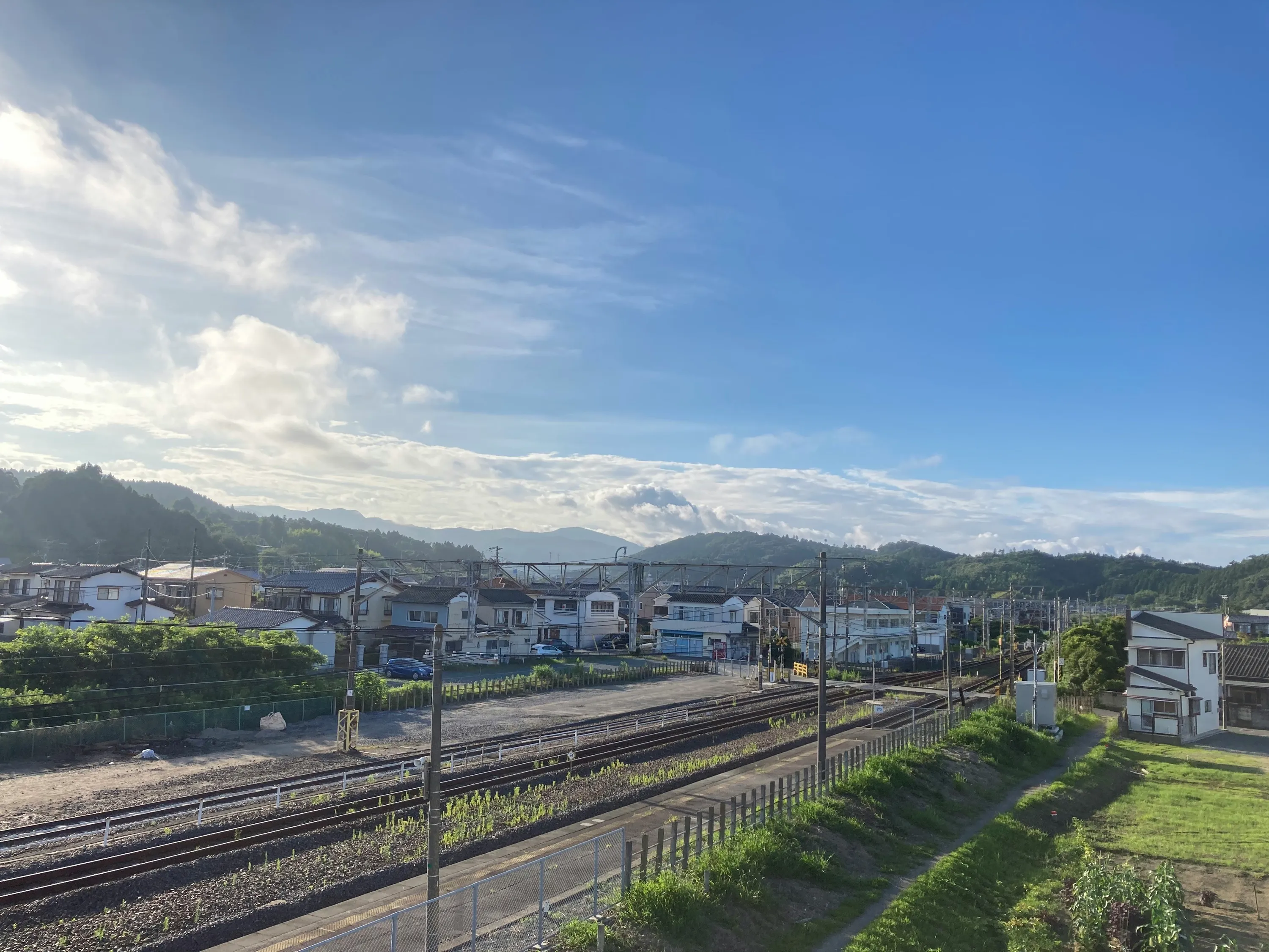 A small town under a wide blue sky, with railway lines and green hills